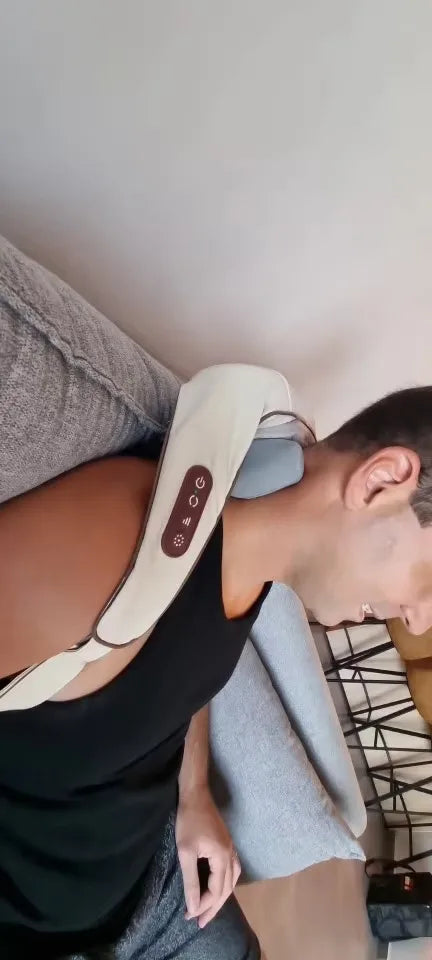 Man relaxing on couch while using TheraPexa cordless neck and shoulder massager with ergonomic arm loops and control panel visible.